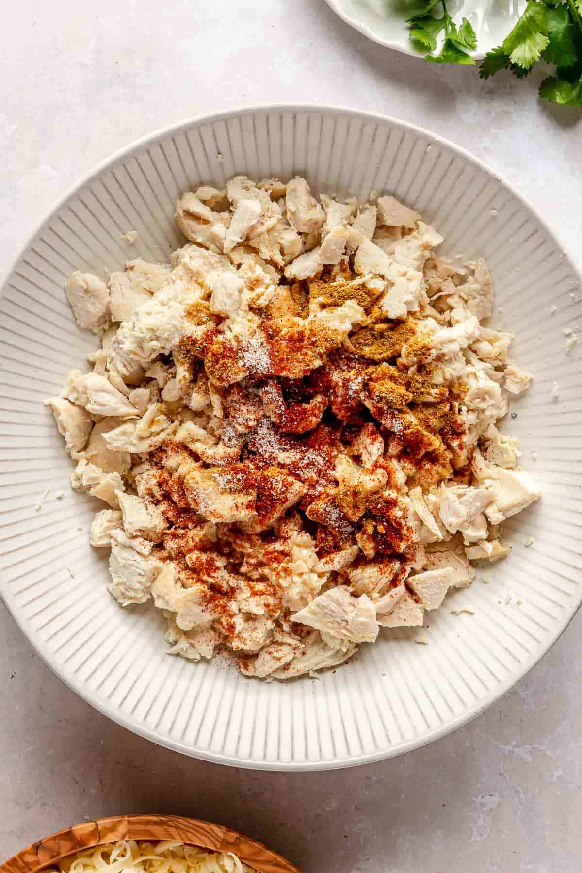 Adding spices to chopped chicken in a bowl.