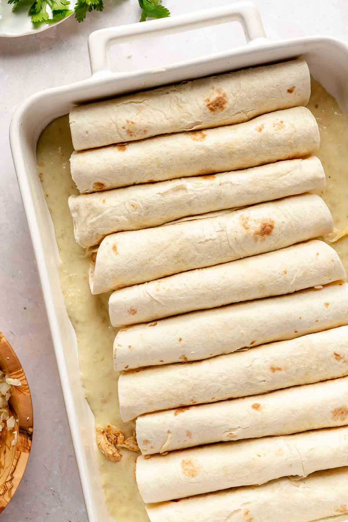 Rolled tortillas in a pan on a creamy sauce.