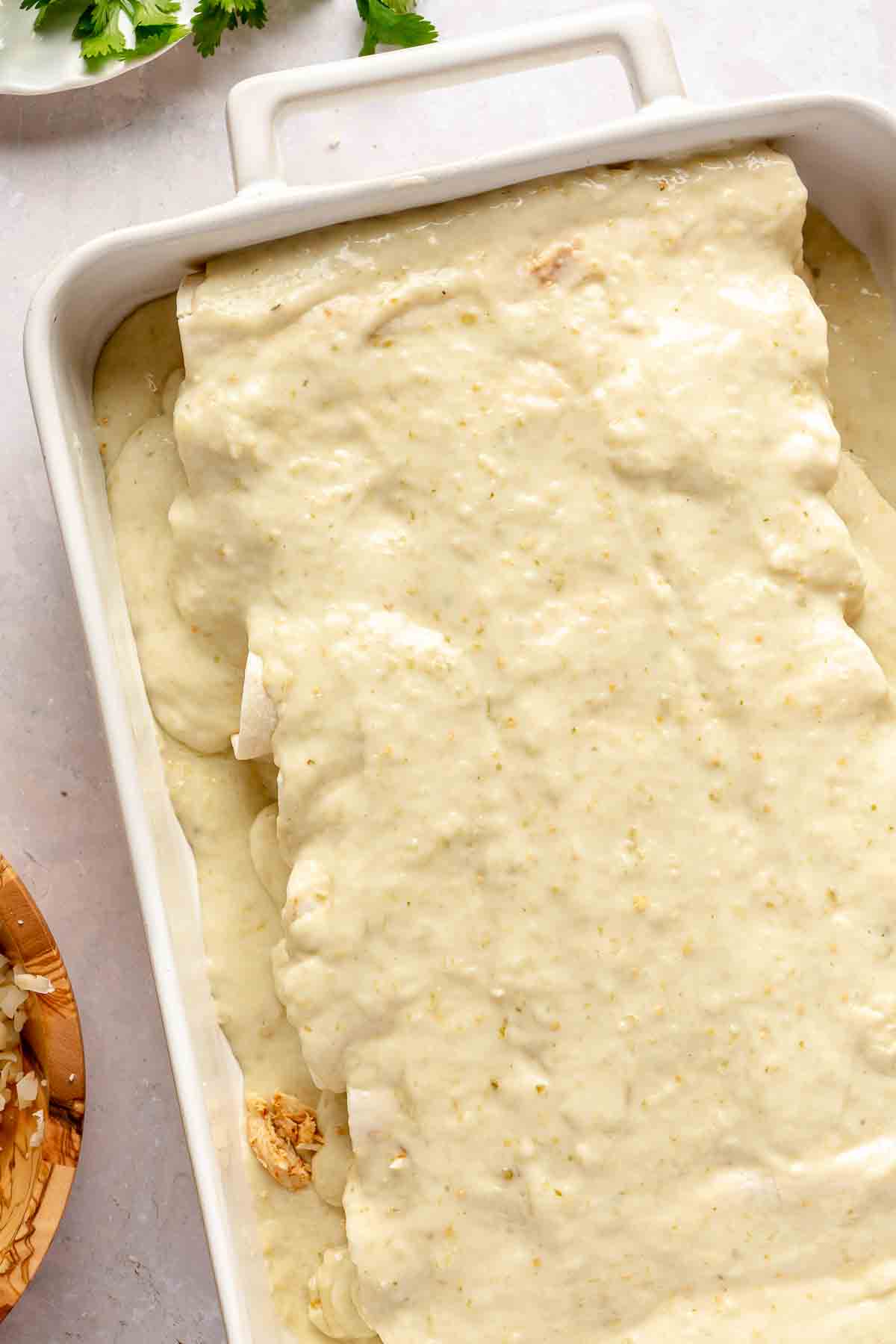 Rolled tortillas layered in a dish with creamy sauce.