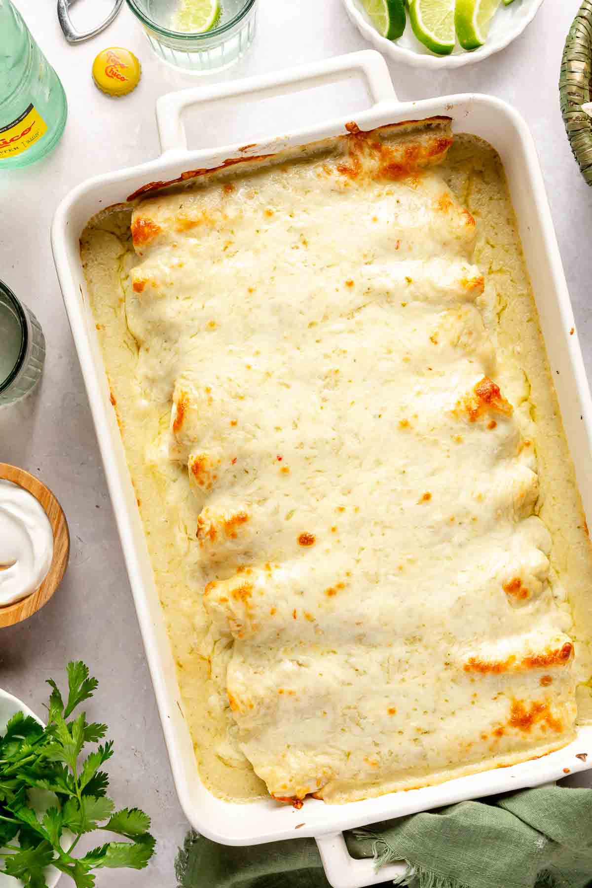 Baked enchiladas verdes with a creamy sauce in a white casserole dish.