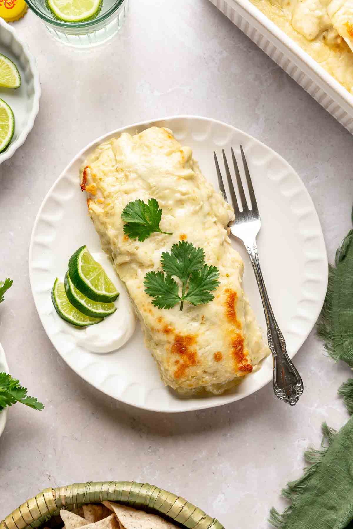 A serving of enchiladas verdes on a white plate with lime and sour cream.