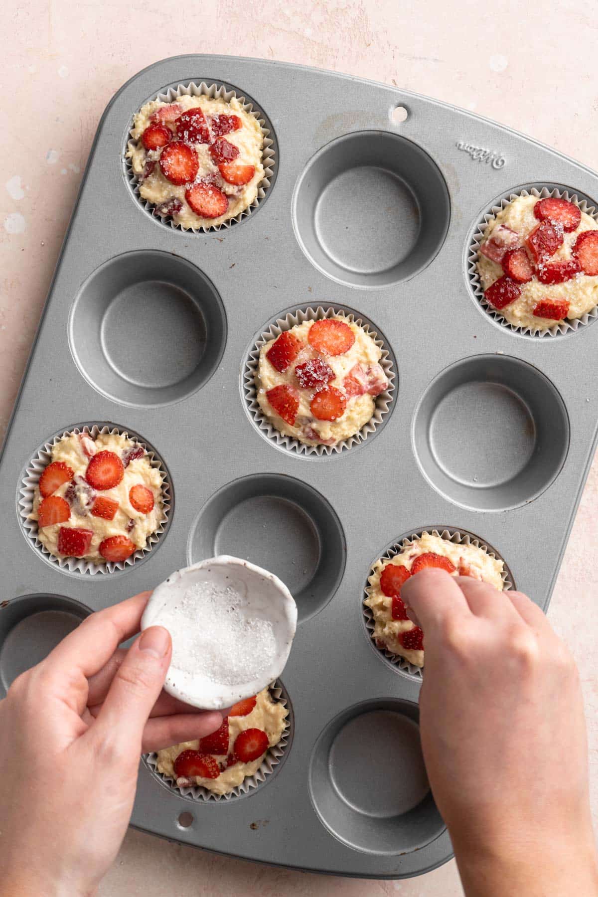 Adding diced strawberries over the tops of the muffins.