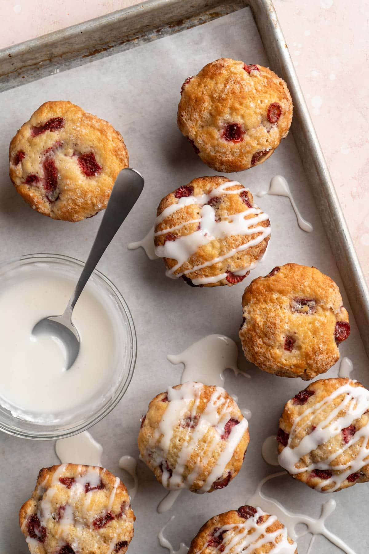 Drizzling glaze over strawberry muffins on a pan.