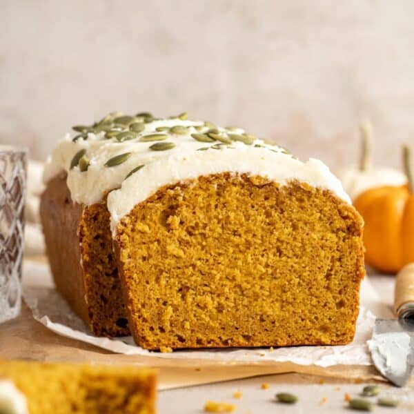 A sliced loaf of vegan pumpkin bread with cream cheese frosting.