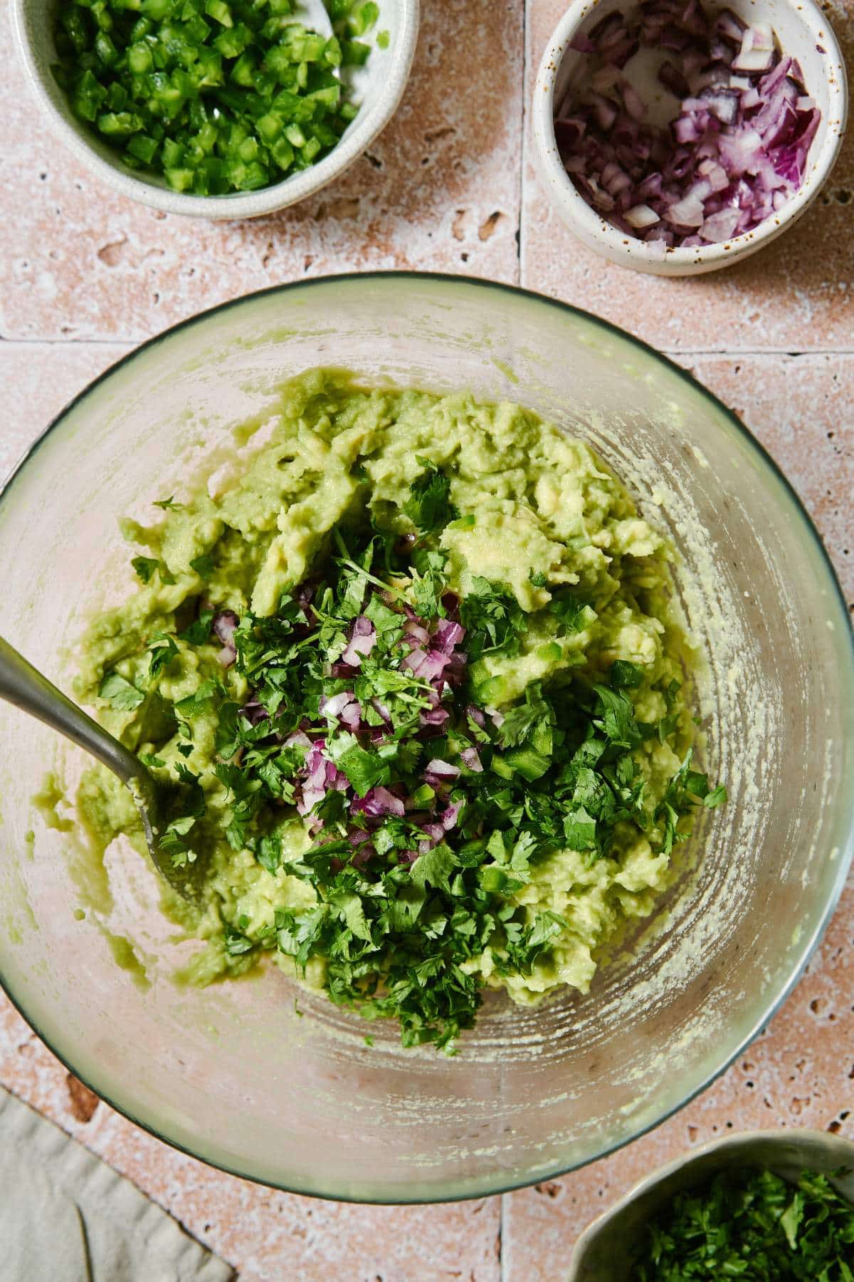 Mixing fresh cilantro and red onion into mashed avocado.