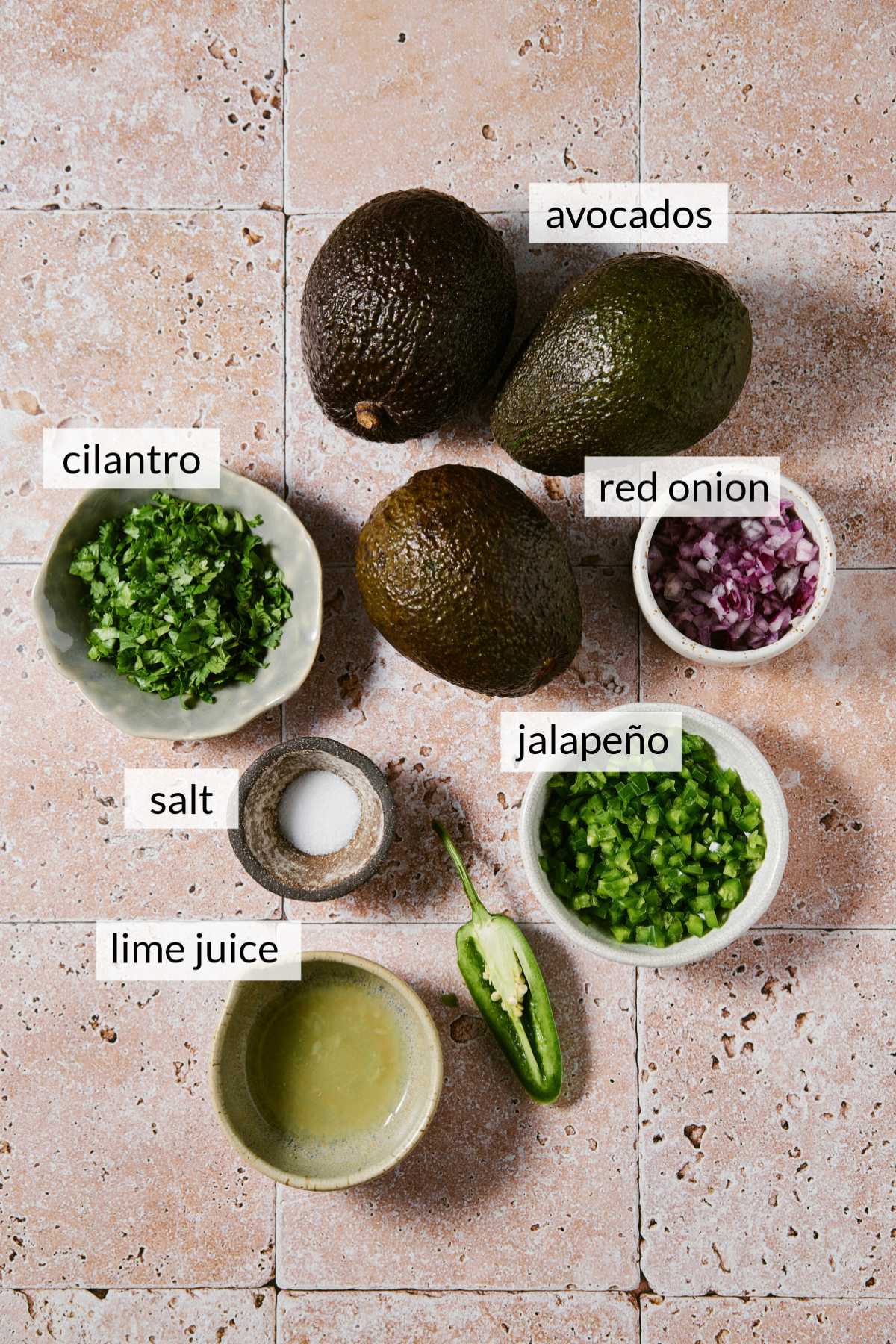 Avocados with bowls of minced cilantro, jalapeños and red onion.