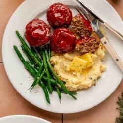 White plate with mini meatloaves, mashed potatoes and green beans.