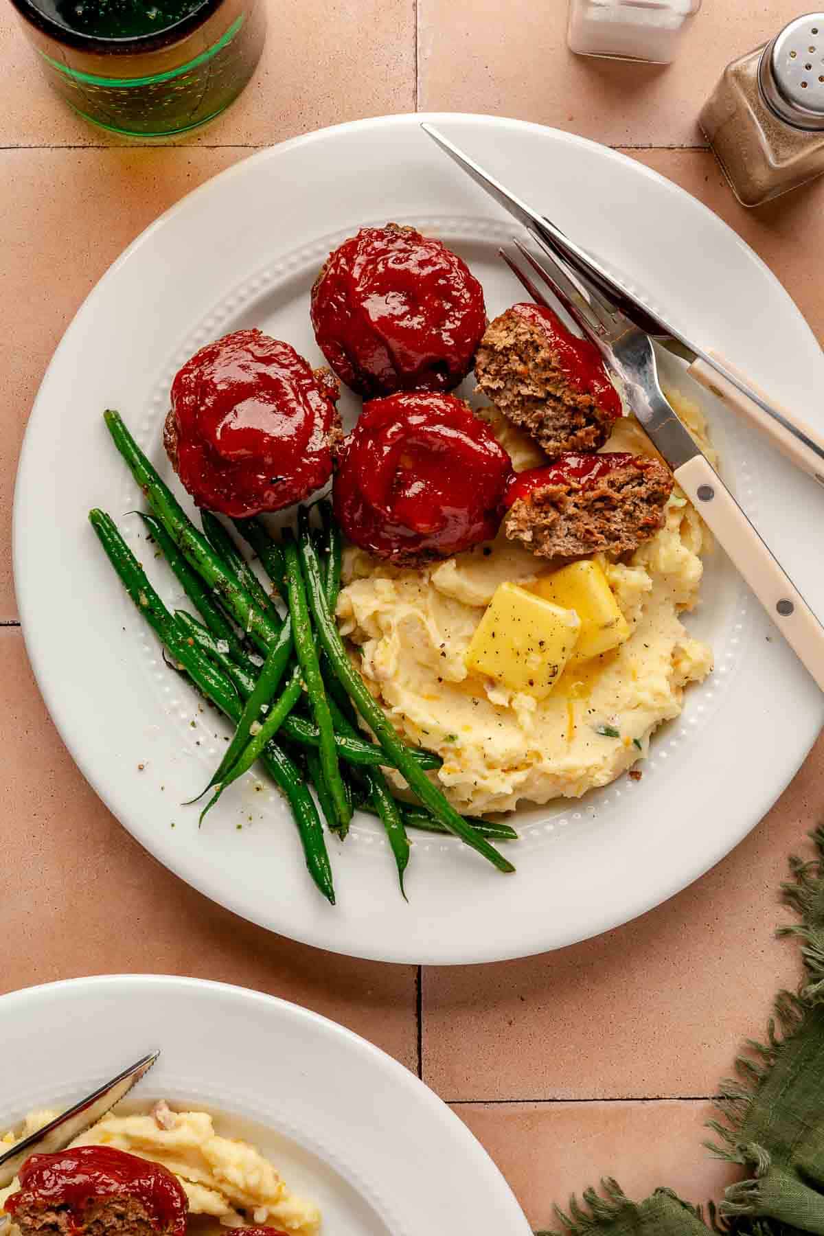 White plate with mini meatloaves, mashed potatoes and green beans.