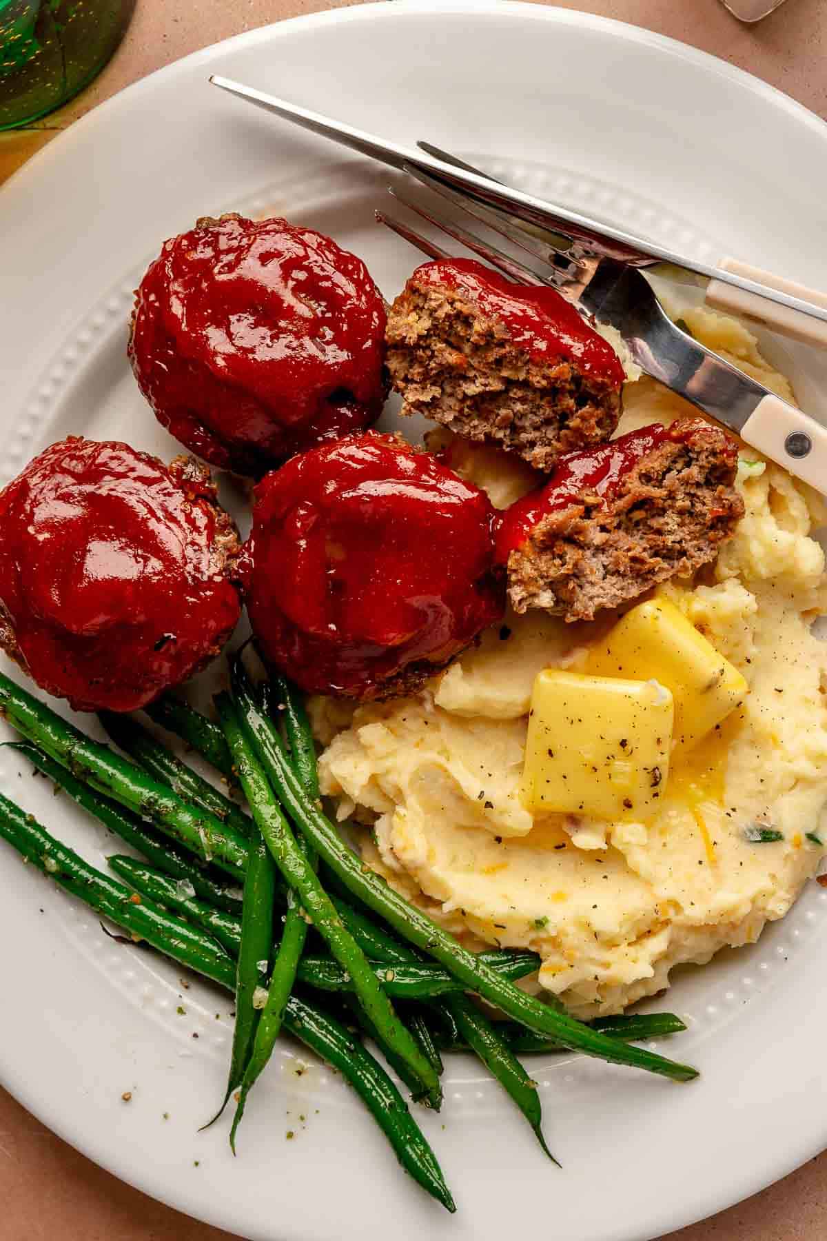 Mini meatloaves served with mashed potatoes and green beans on a white plate.