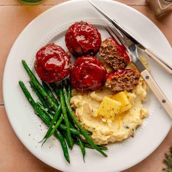 White plate with mini meatloaves, mashed potatoes and green beans.