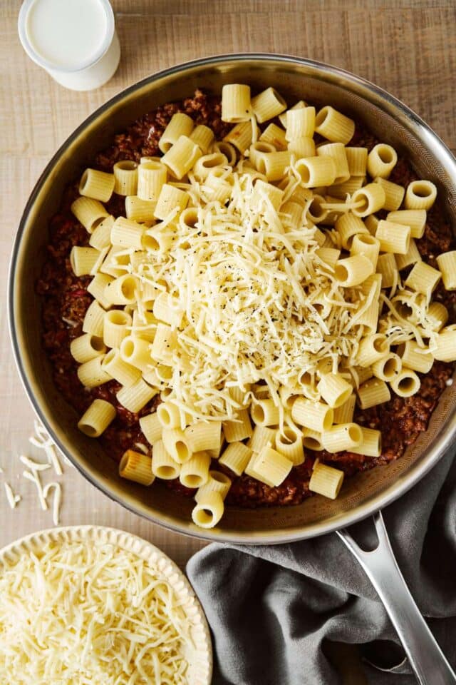 Adding pasta and cheese to ground beef.