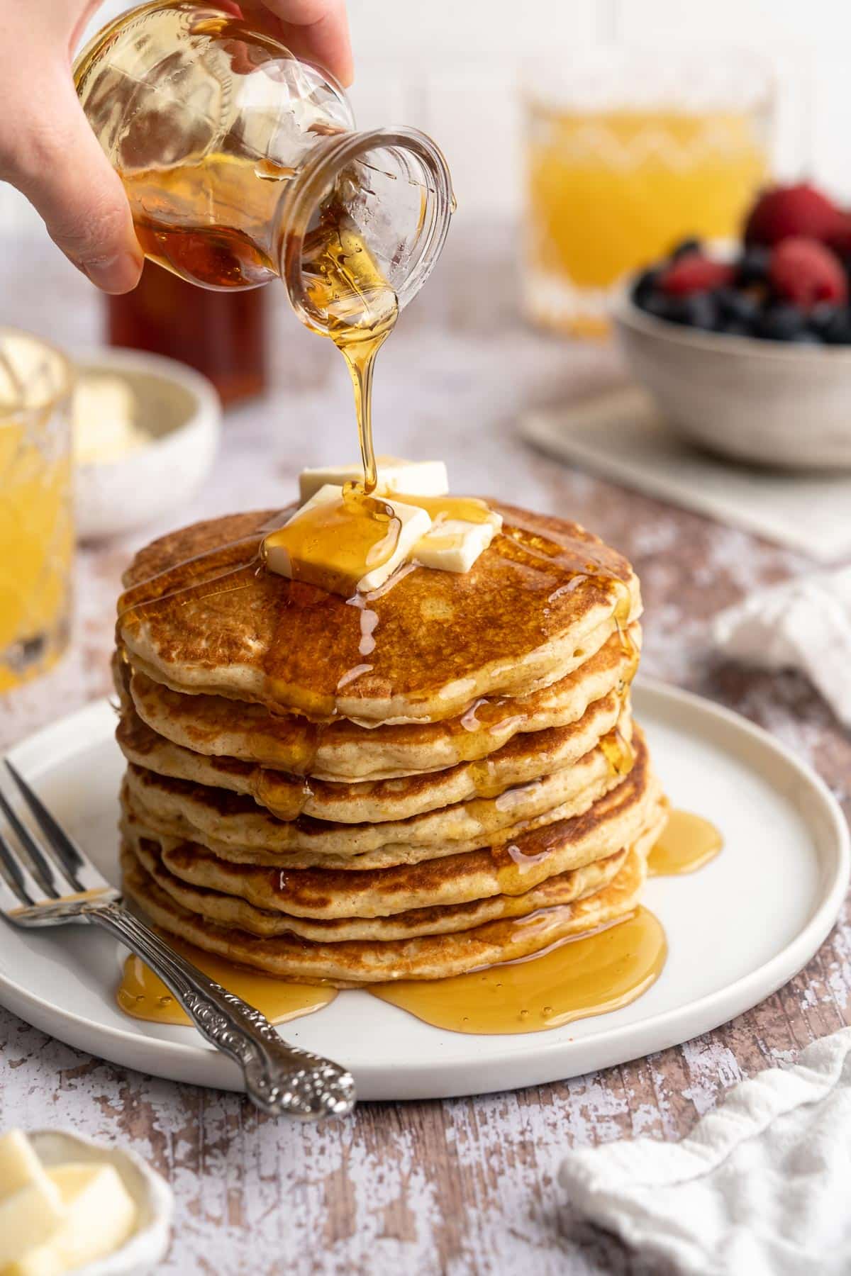 Drizzling maple syrup over a stack of whole grain pancakes.