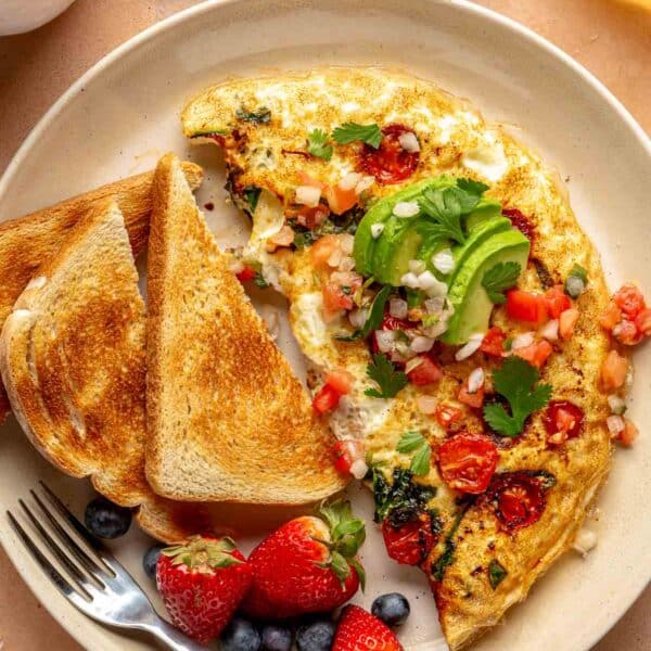 Egg white omelet topped with avocado and served with toast on a plate.