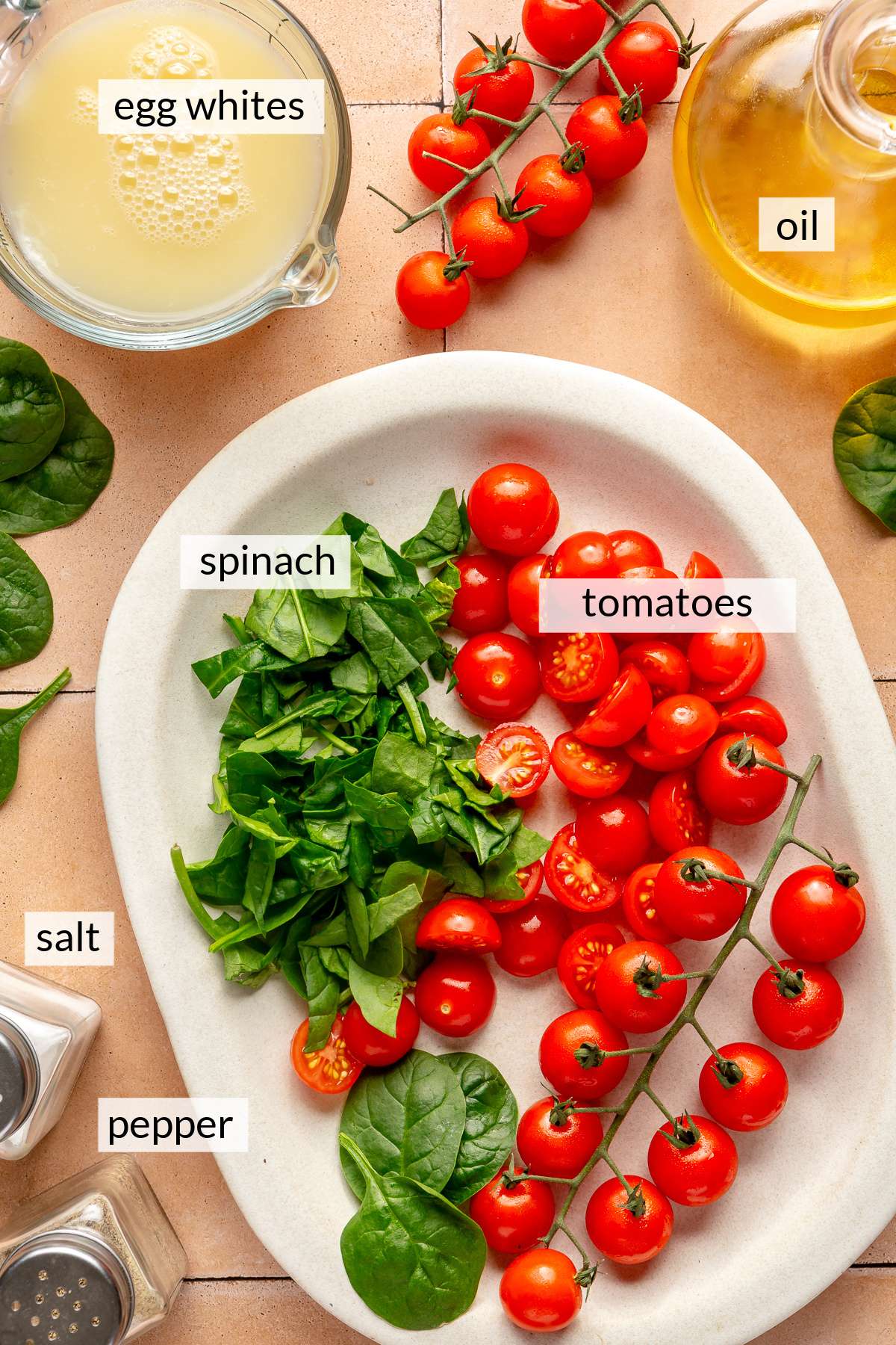 Fresh tomatoes and spinach on a plate near egg whites and oil.