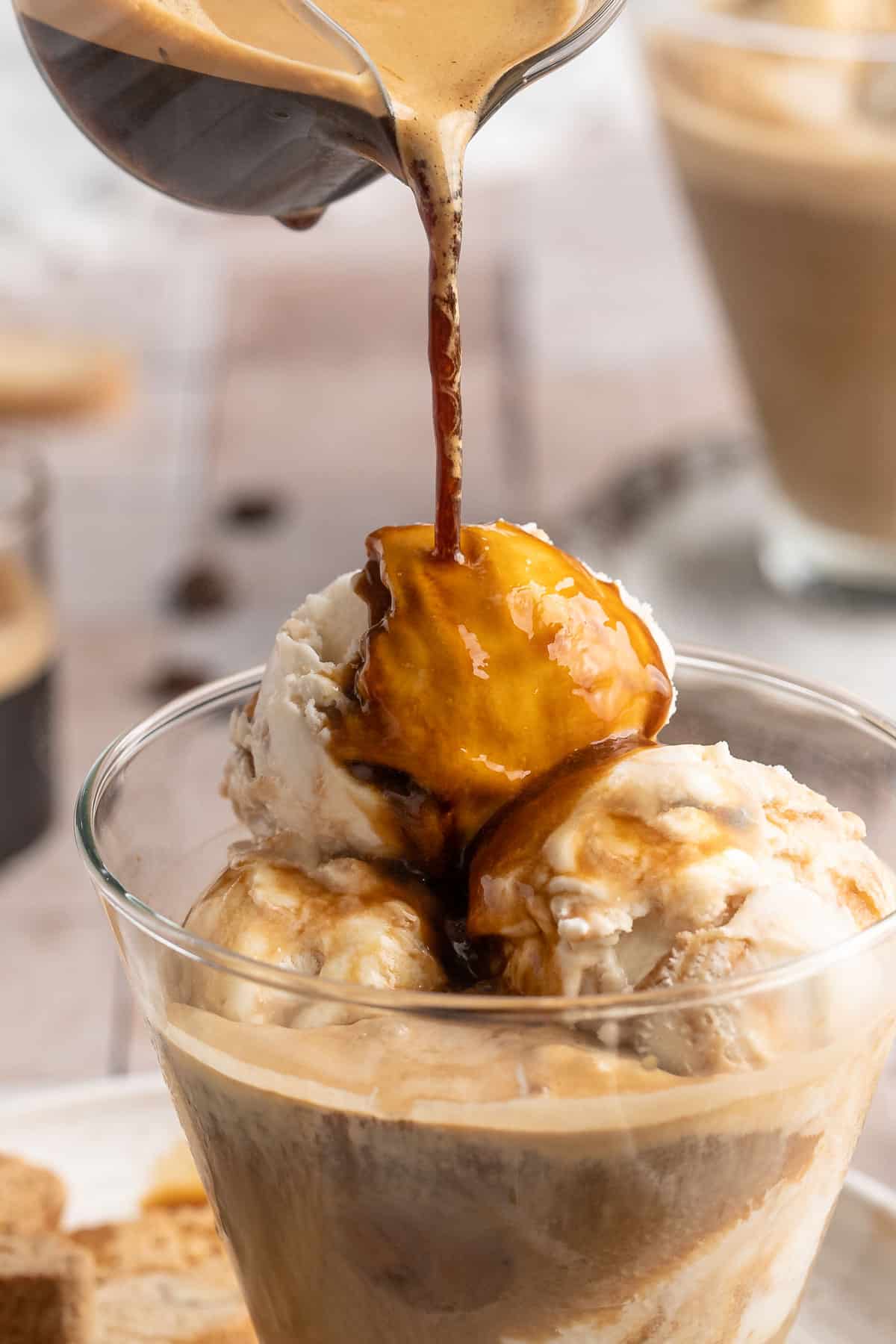 Pouring espresso over scoops of ice cream in a glass.