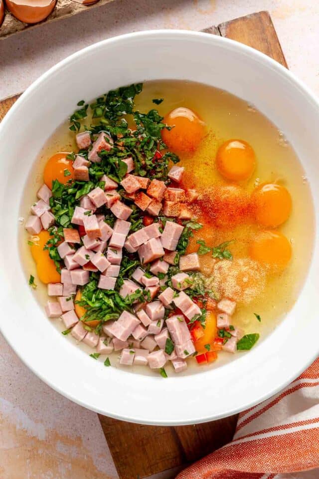 Adding eggs, chopped ham, spinach and red bell pepper to a bowl.