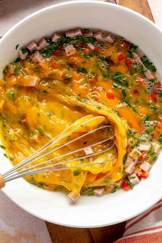 Whisking eggs with meat and veggies in a large white bowl.