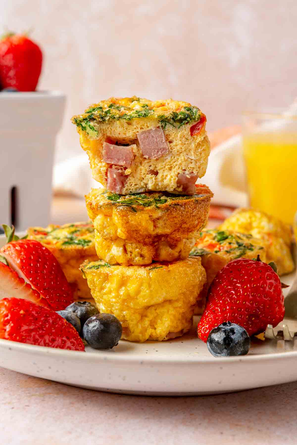 There egg muffins stacked on a plate with fruit.