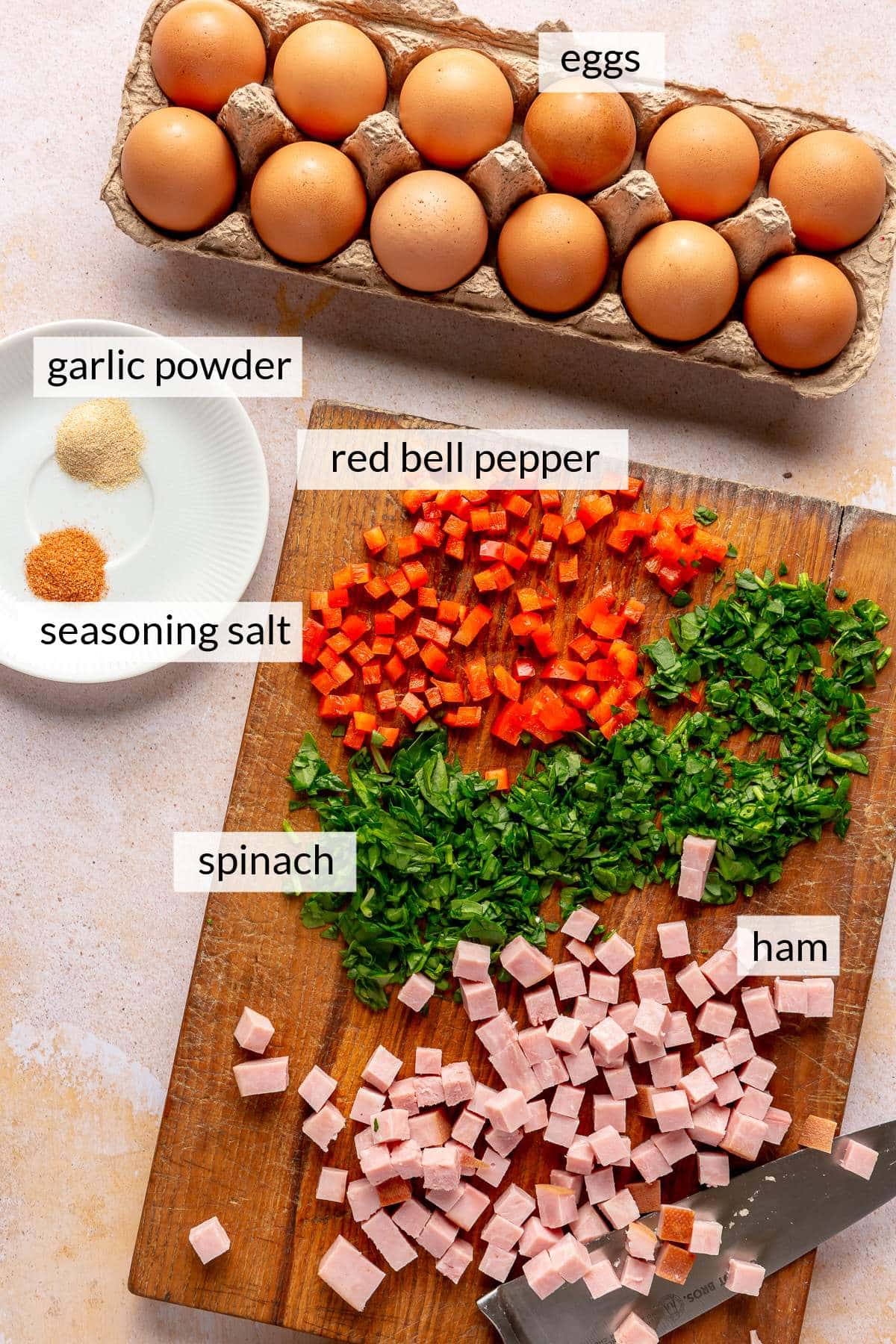 Eggs near a cutting board with chopped bell pepper, ham and spinach.