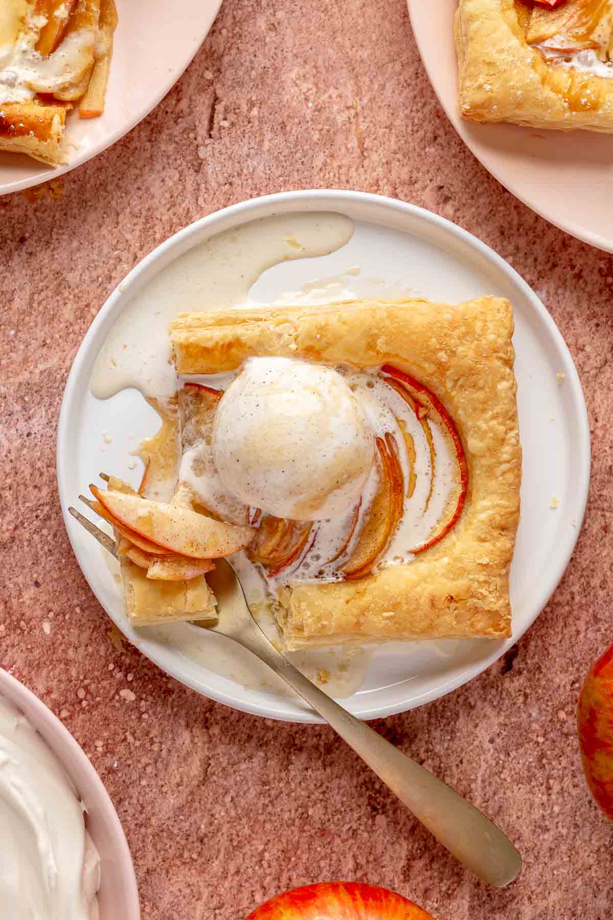 Puff pastry apple tart on a plate with a fork and a scoop of melting vanilla ice cream.