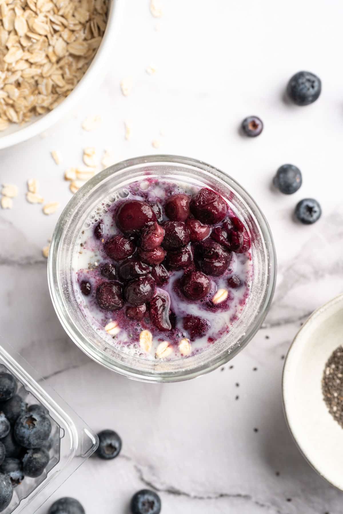 Adding blueberries with oats, milk and chia seeds to mason jar.