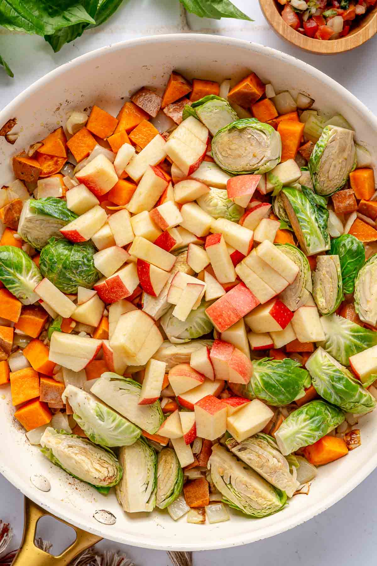 Cooking sweet potato with Brussels sprouts and apple chunks in a large pan.