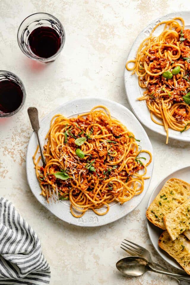 Meat sauce served over spaghetti on white plates with garlic bread.