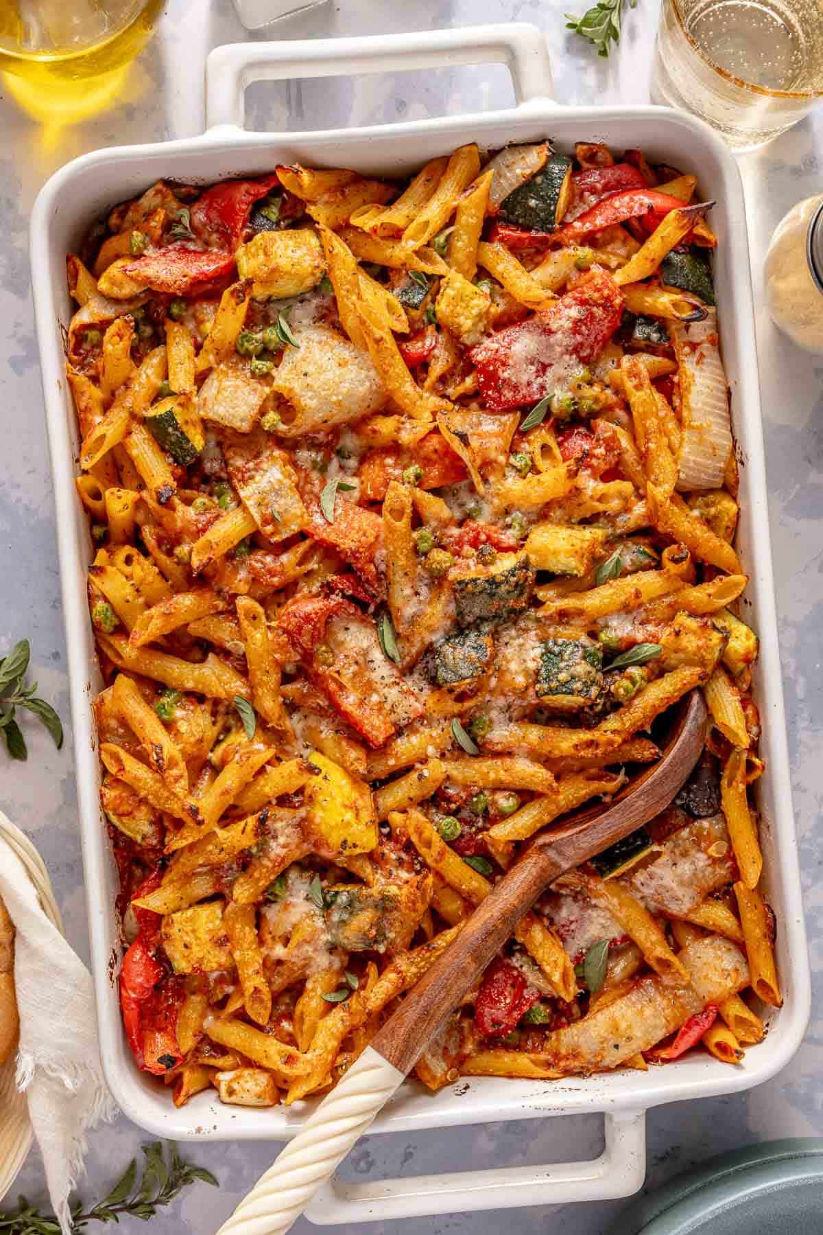 Roasted vegetable pasta in a casserole dish with a serving spoon.