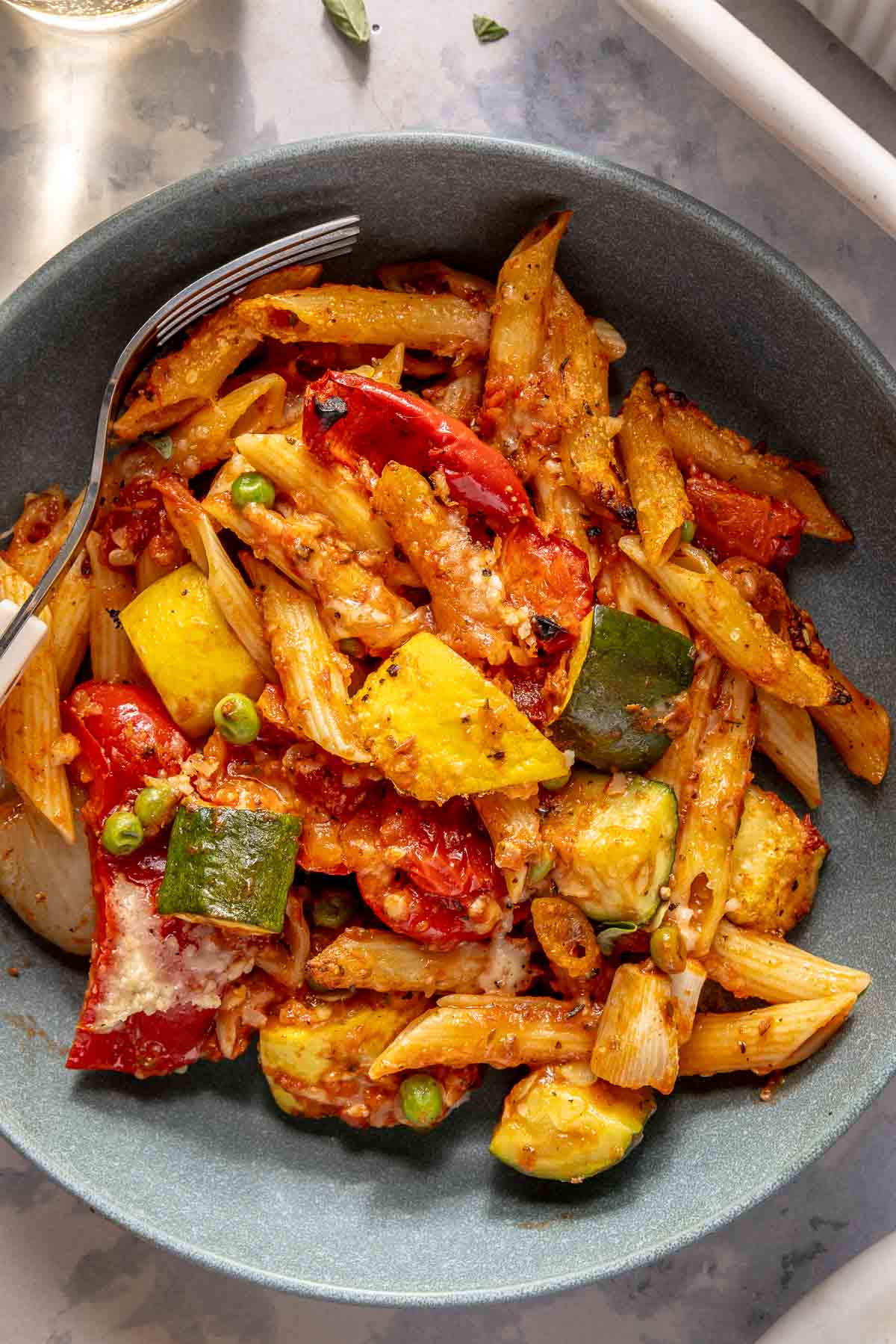 Penne with vegetables in a bowl with a fork.