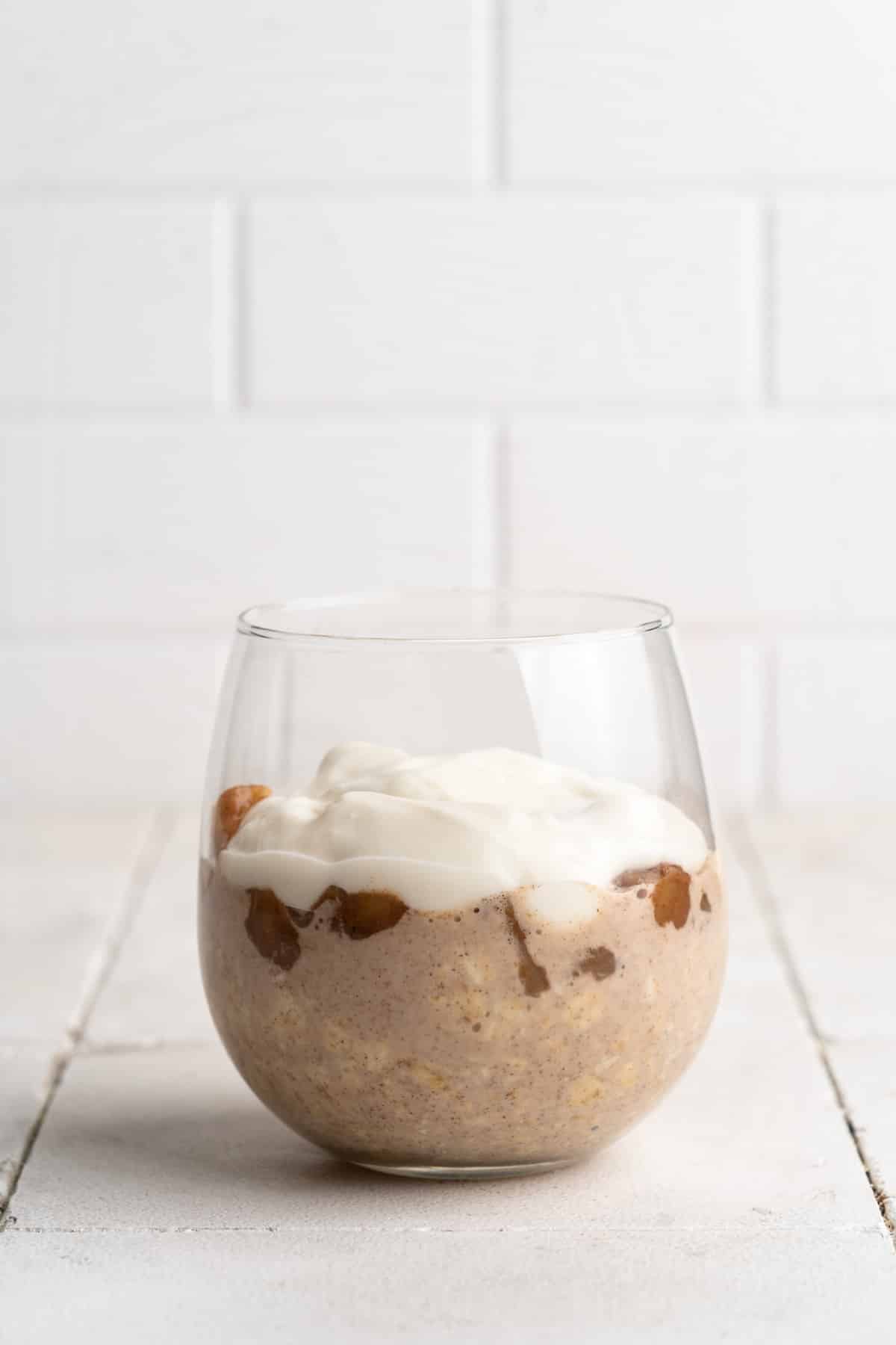 Yogurt added on to of apples and oatmeal in a glass.