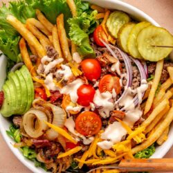 Hamburger bowl topped with sautéed onions, pickles and fries.