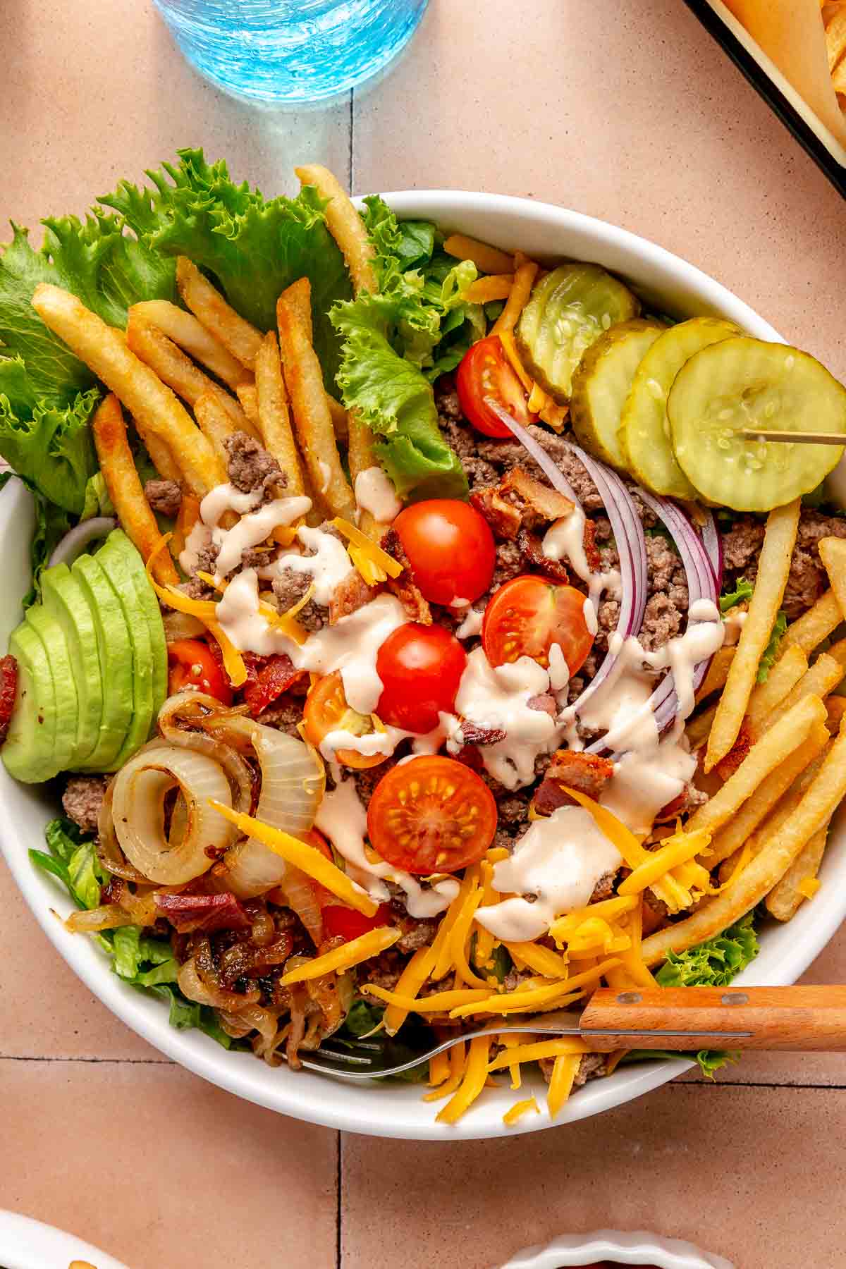 Hamburger bowl topped with sautéed onions, pickles and fries.