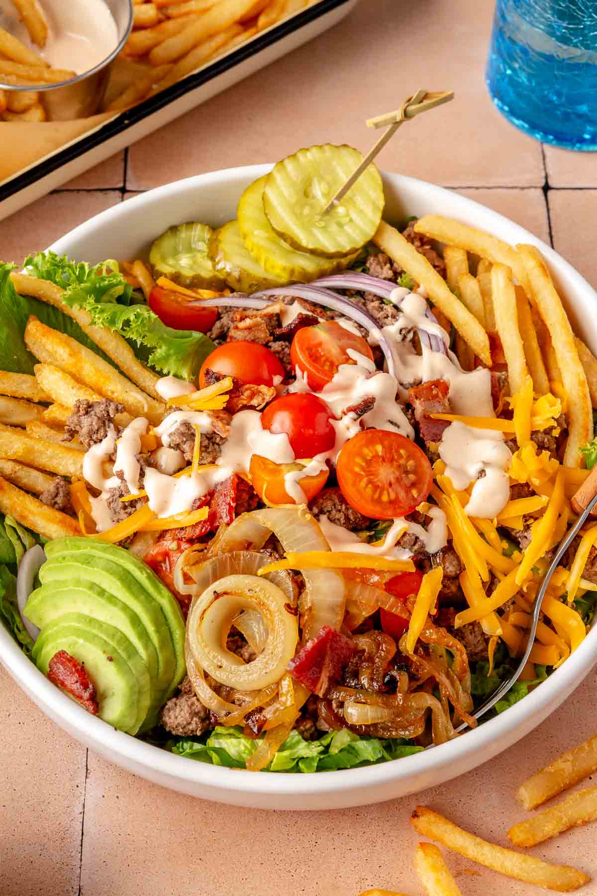 Hamburger bowl made with beef, lettuce, tomato, pickle, sauce and French fries.