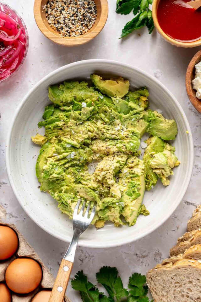 Mashing avocado with a fork in a white bowl.