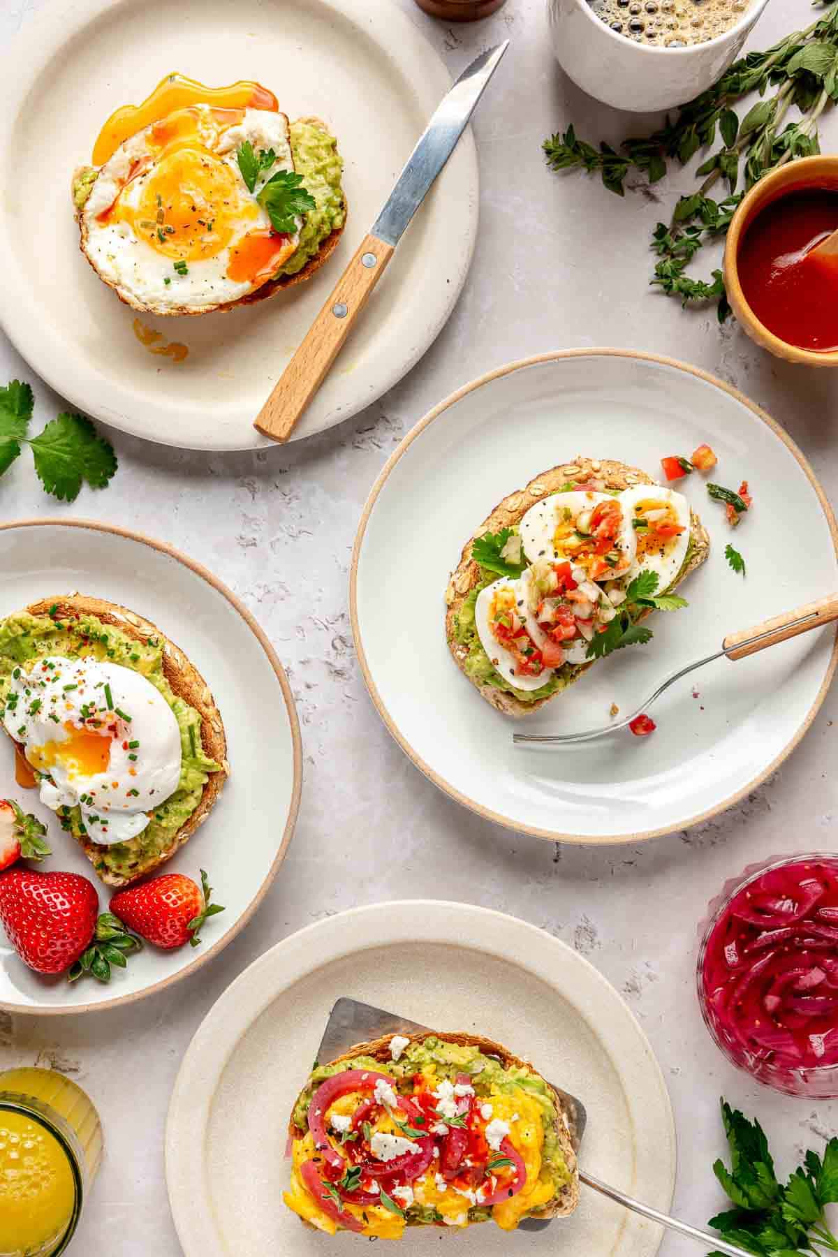 Different types of avocado toast with egg options served on white plates.