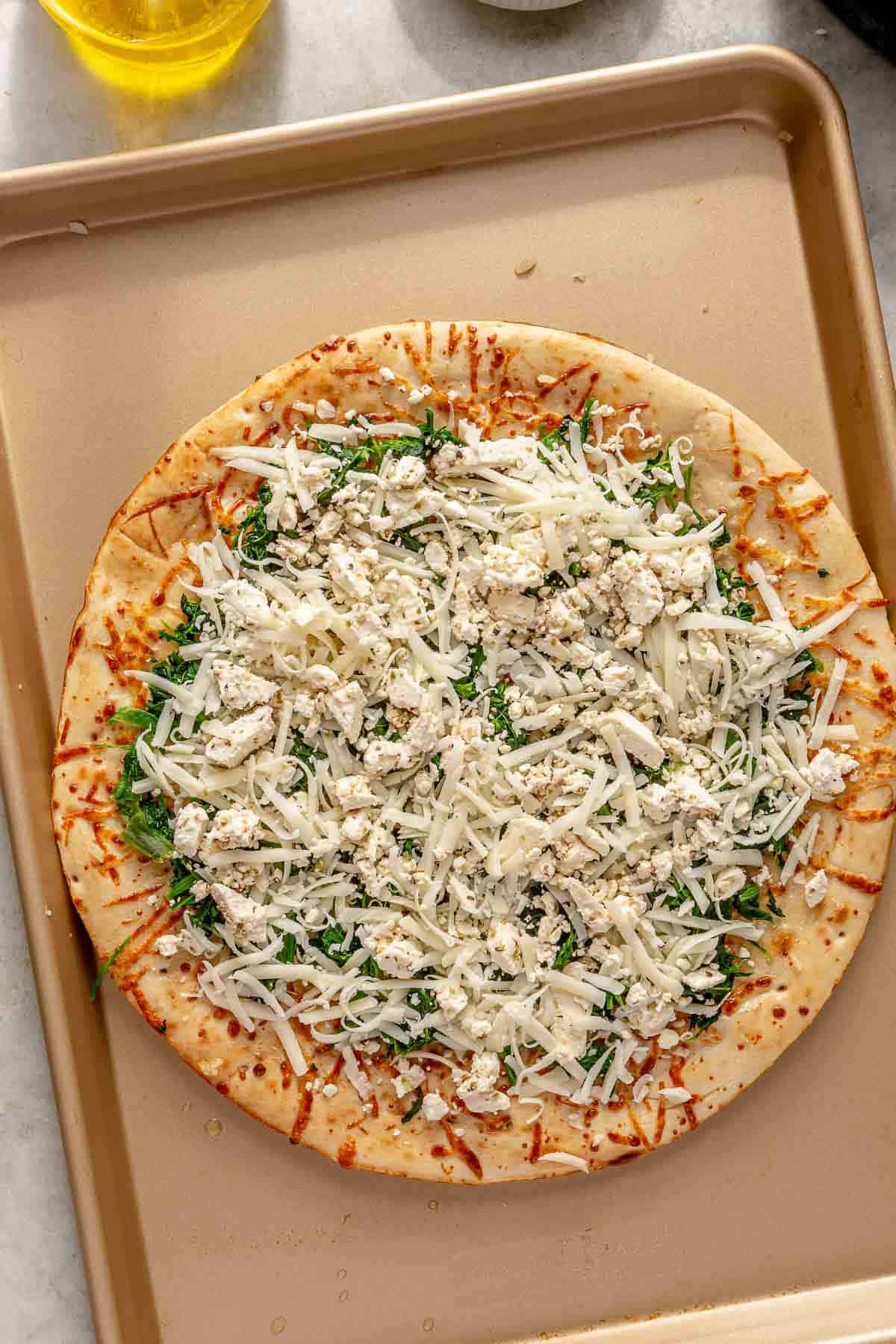 Uncooked pizza topped with spinach and cheese.