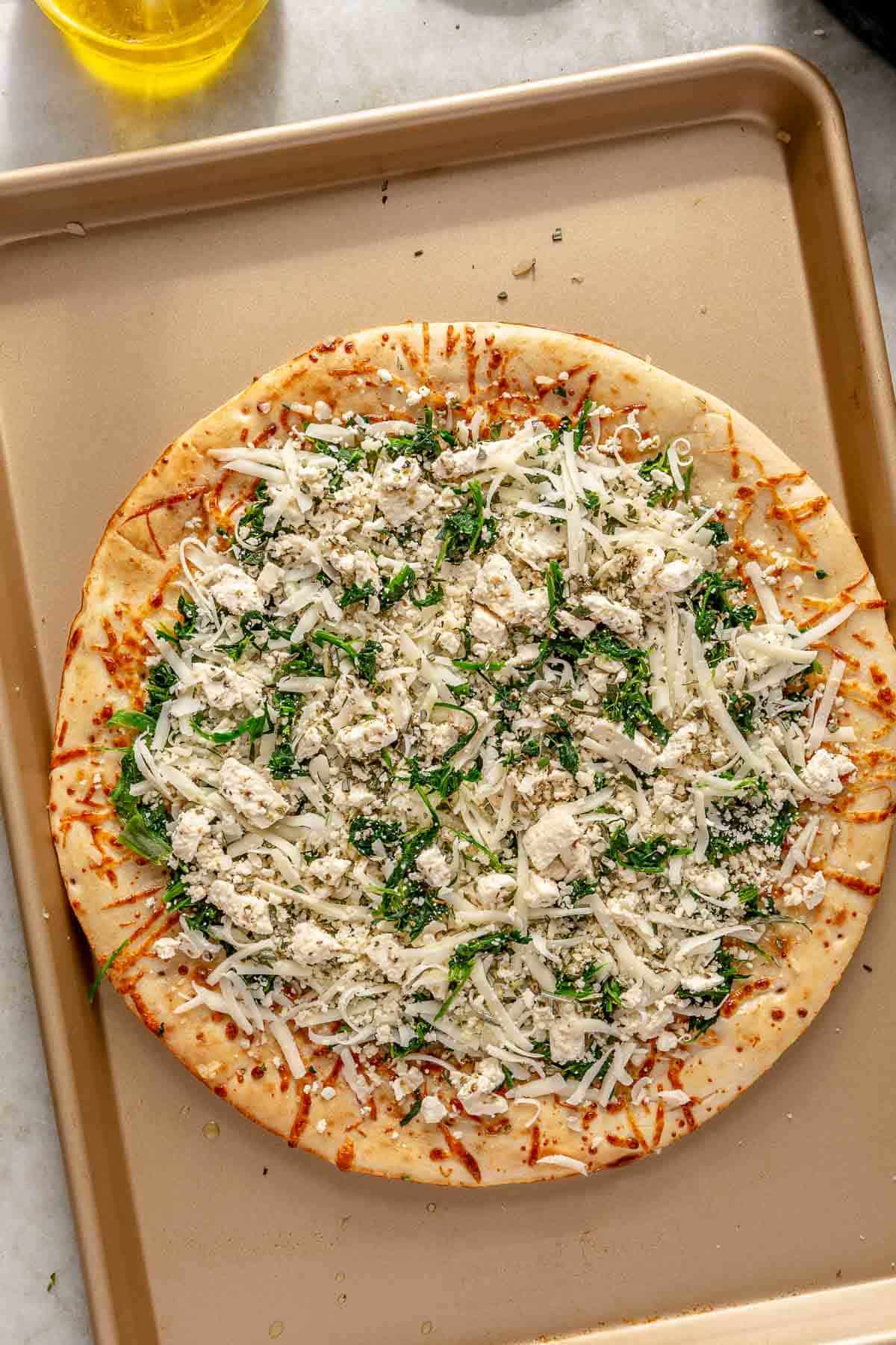 White pizza before being baked topped with spinach, cheese and rosemary.