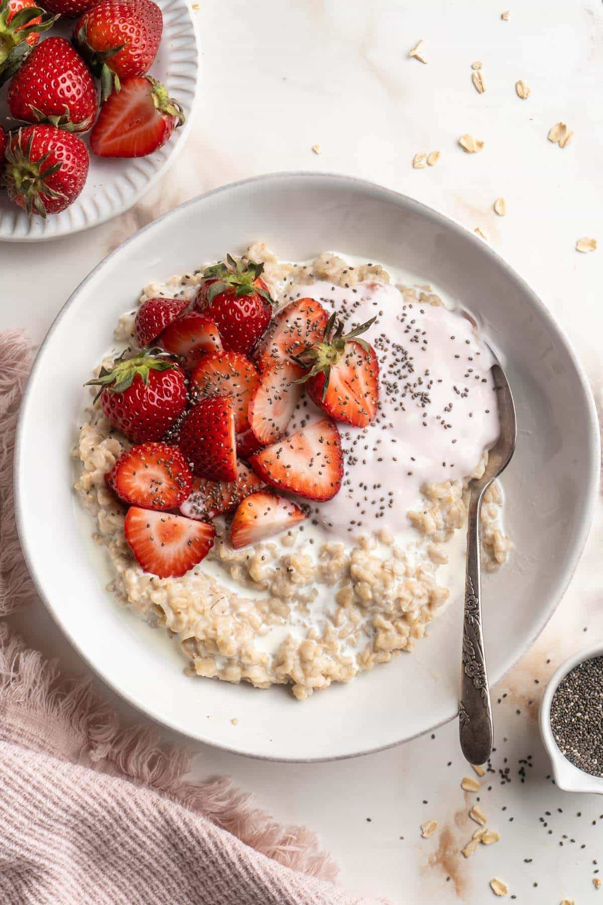 Oatmeal in a white bowl with strawberries and strawberry yogurt.