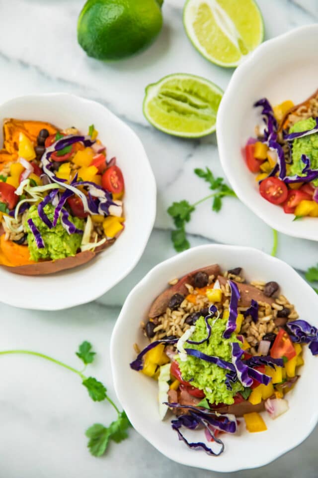 overhead of Healthy Sweet Potato Burrito Bowls in white bowls, topped with guacamole and purple cabbage