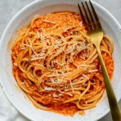 Spaghetti served with roasted red pepper sauce in a white bowl with a fork.