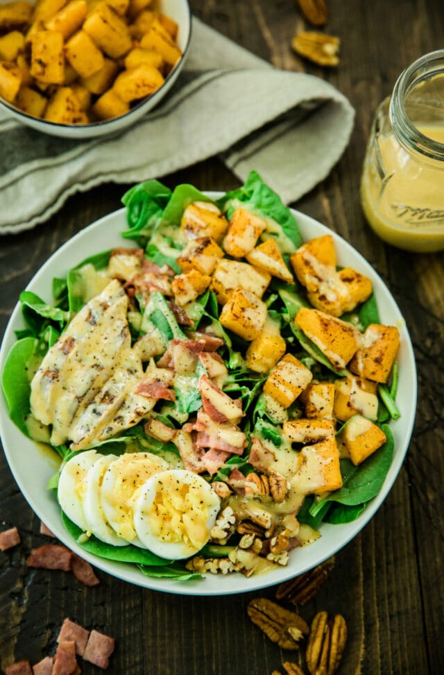 overhead photo of the Healthy Harvest Cobb Salad served in a white bowl with a side of dressing in a glass jar