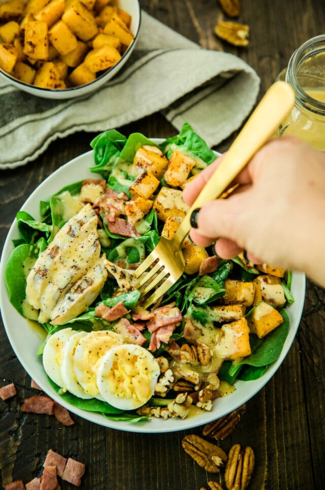 overhead view of woman's hand holding a gold fork over the Healthy Harvest Cobb Salad