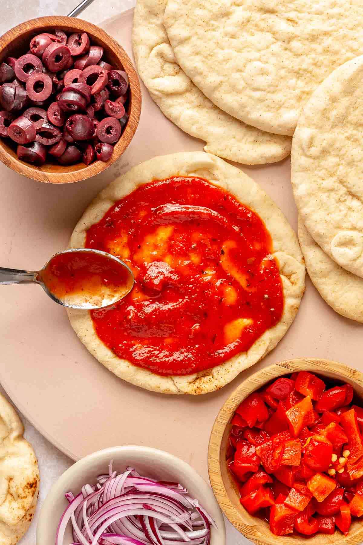 Using a spoon to spread pizza sauce over a pita.