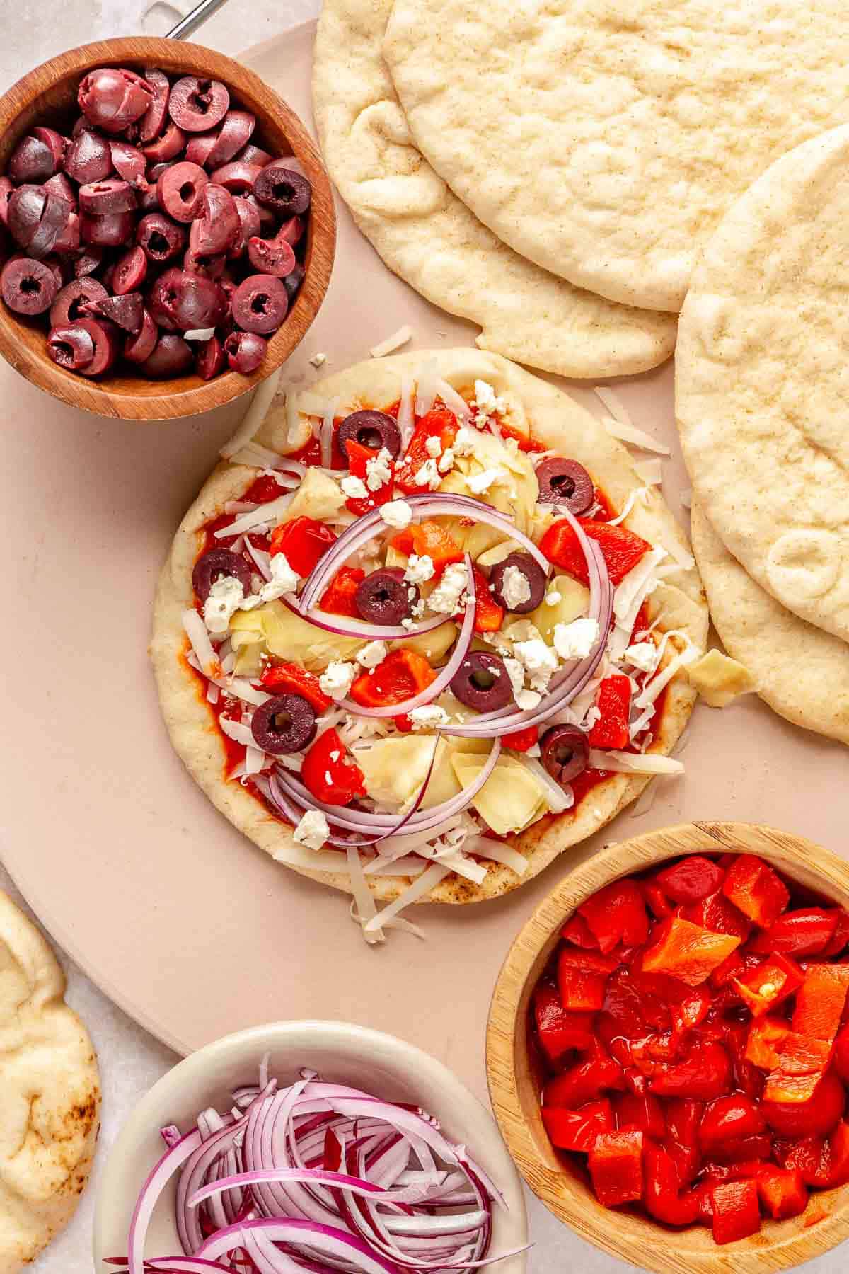 Pita pizza topped with red bell pepper, red onion and black olives.