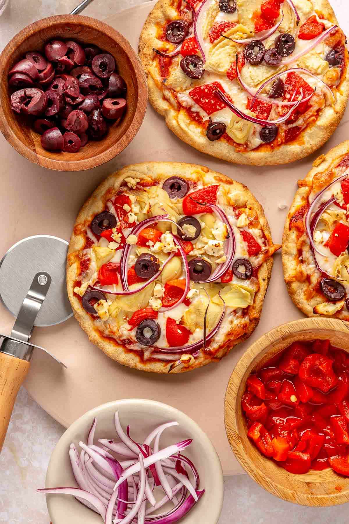 Baked pita pizzas on a pizza stone near a pizza cutter.