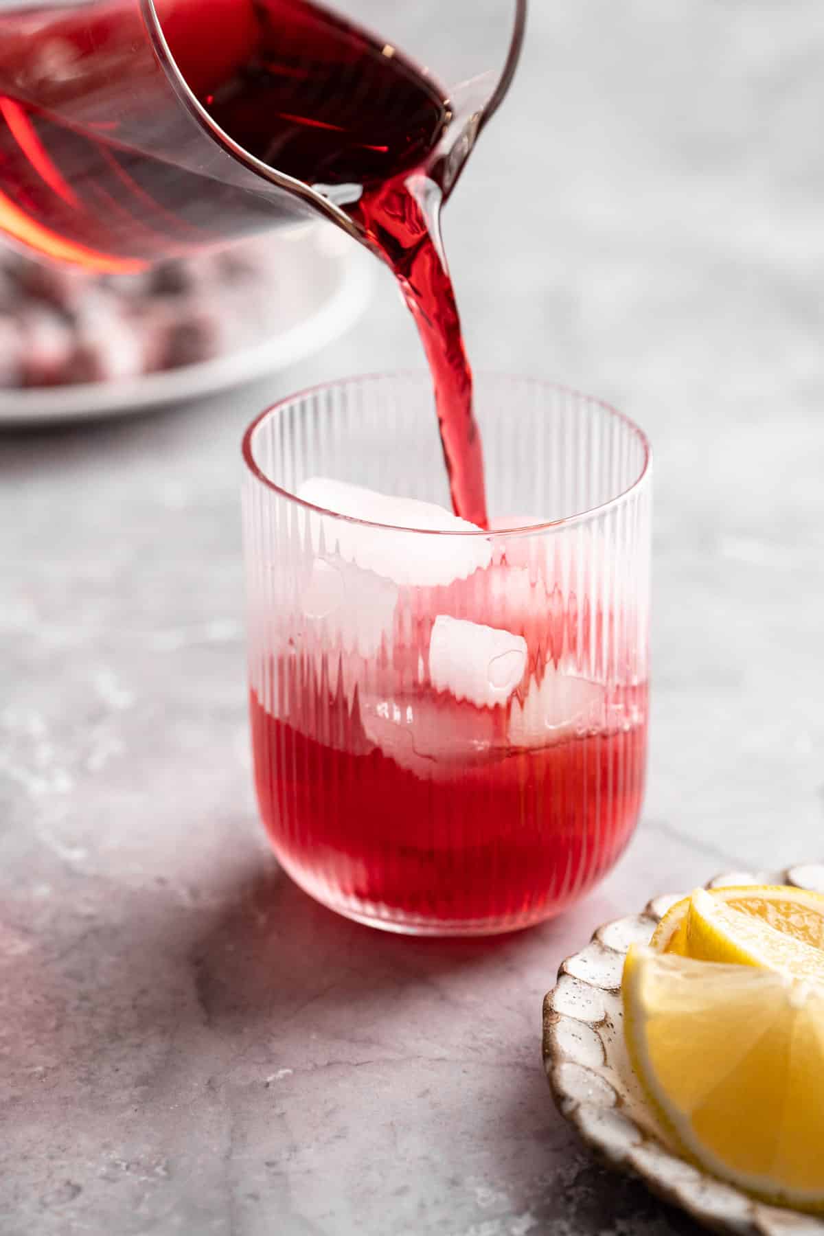 Pouring cranberry juice into a small glass of ice.