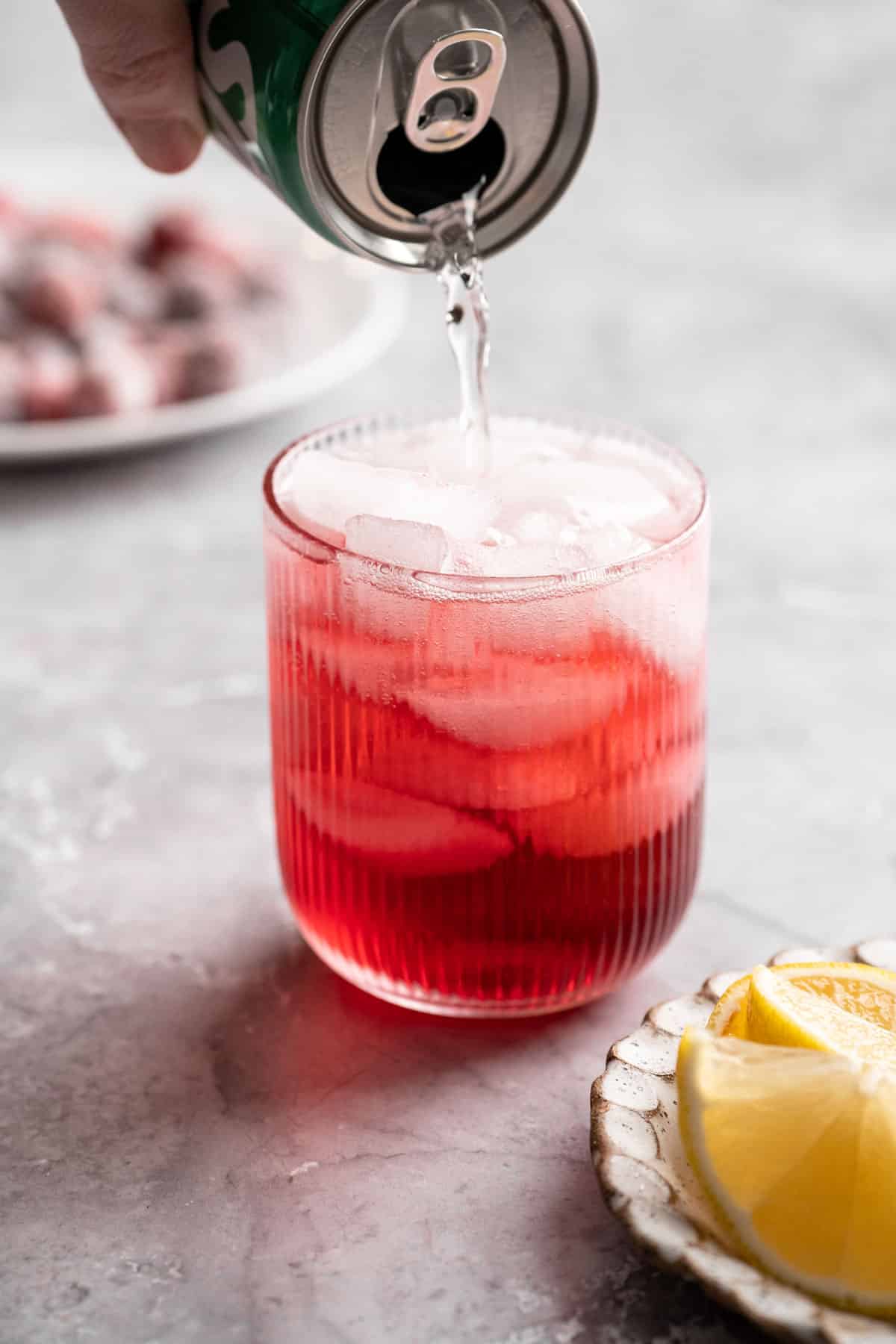 Pouring sprite into a glass with ice and cranberry juice.