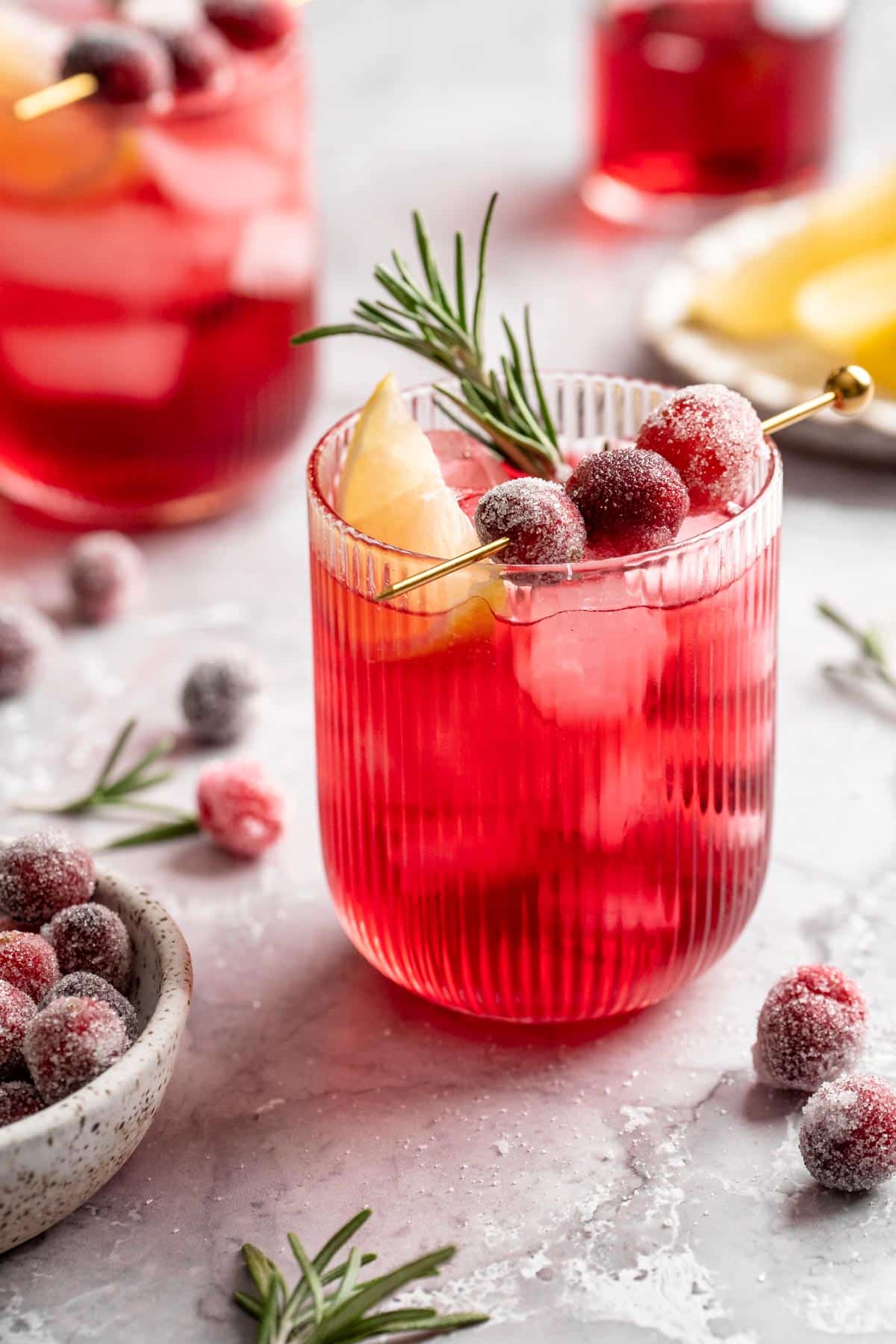 Cranberry cocktail garnished with sugared cranberries, a lemon slice and rosemary.