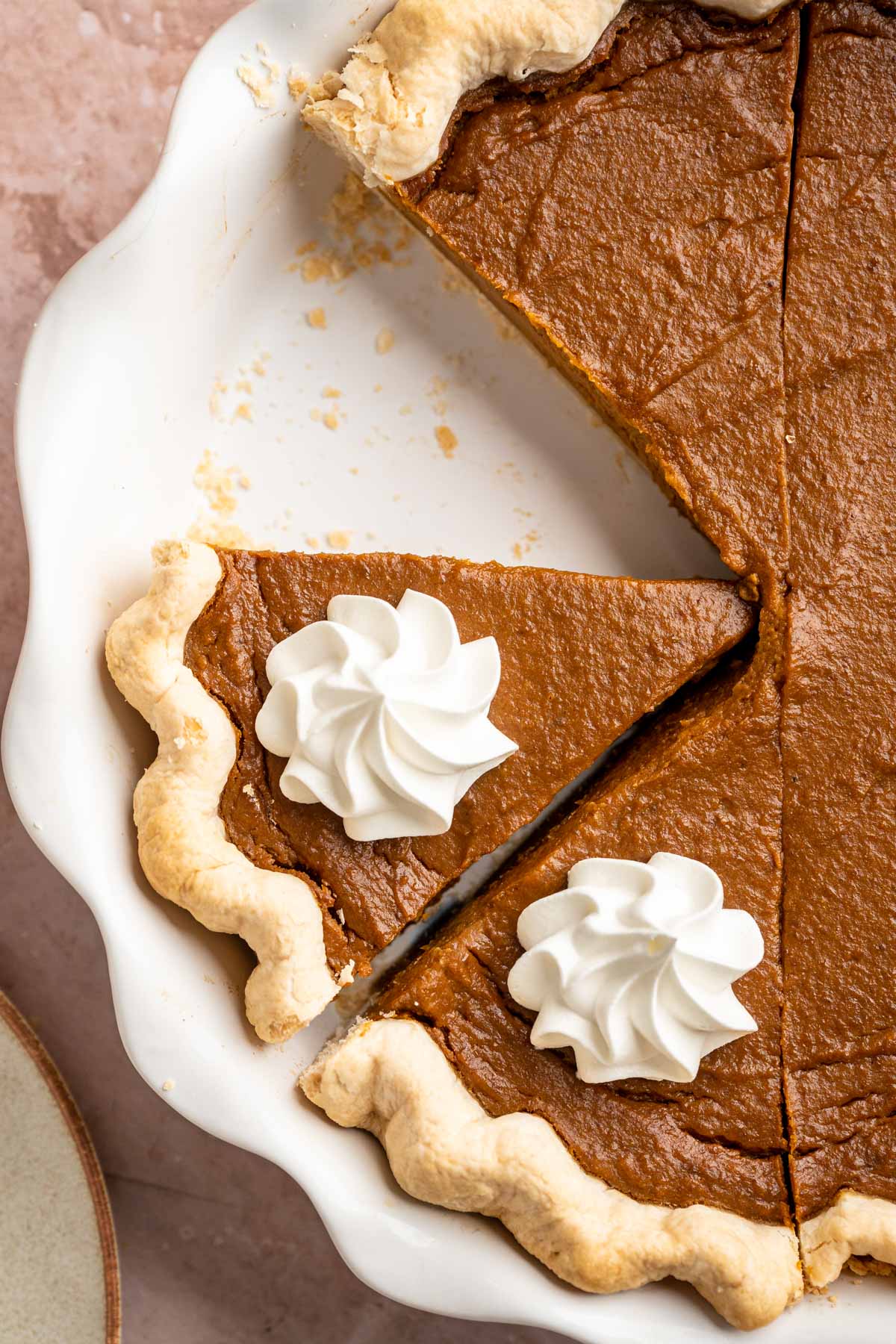 Pumpkin pie sliced in a pie plate and topped with whipped cream.