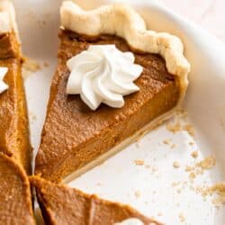 Slice of pumpkin pie in a pie plate topped with whipped cream.